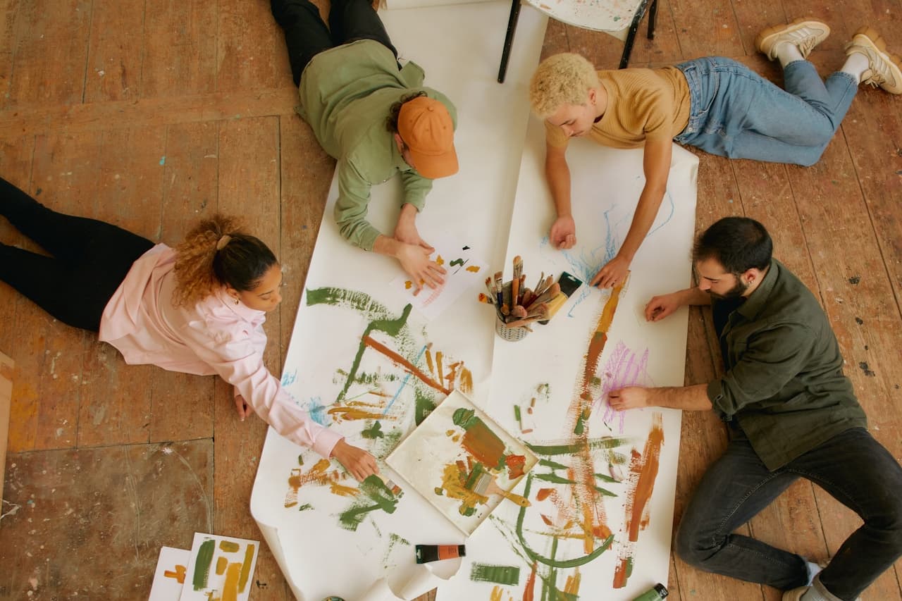 Four people collaborating on artwork around a table in a studio, viewed from above